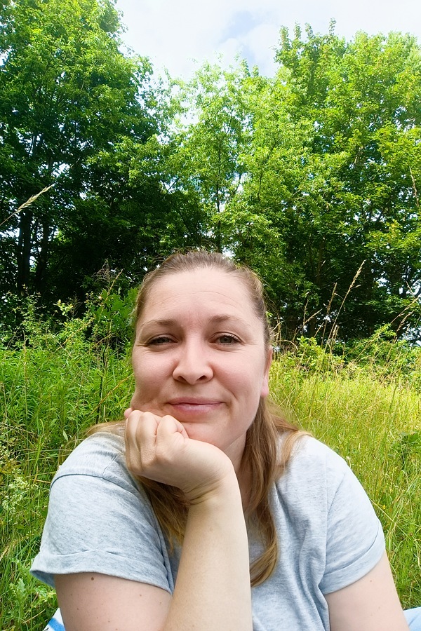 Ich, wie ich auf einer Wiese sitze und in die Kamera schaue