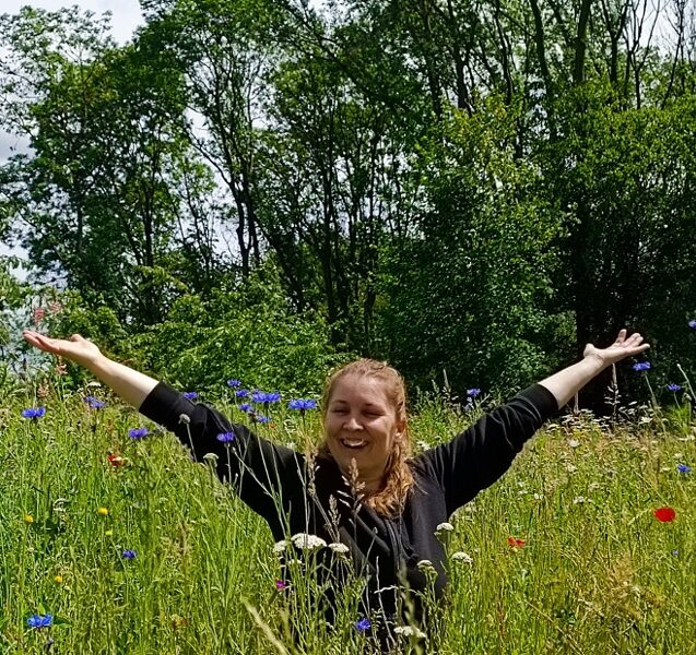 Ich sitze in einer Wiese und hebe die Arme Richtung Himmel