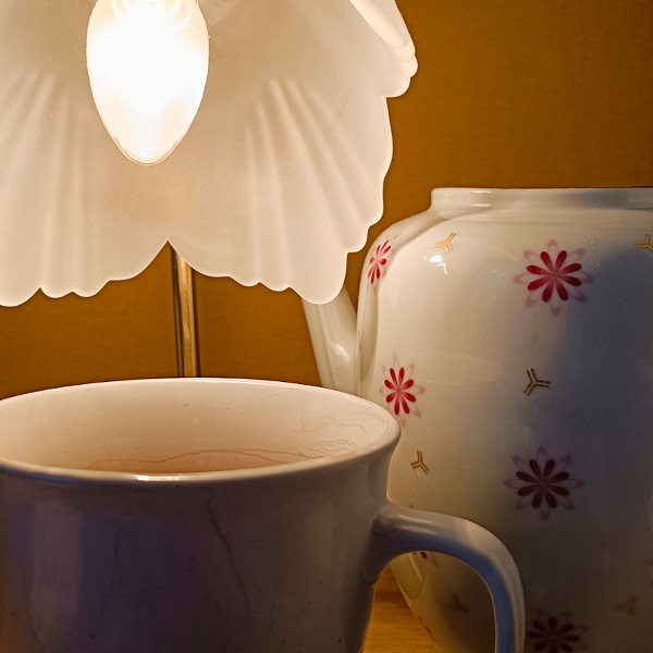 Eine Tasse und eine Kanne Tee, die unter einer Blütenlampe stehen.