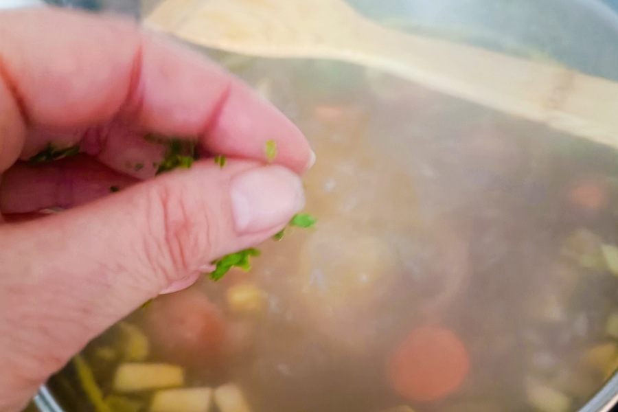 Finger streuen Petersilie in eine Suppe